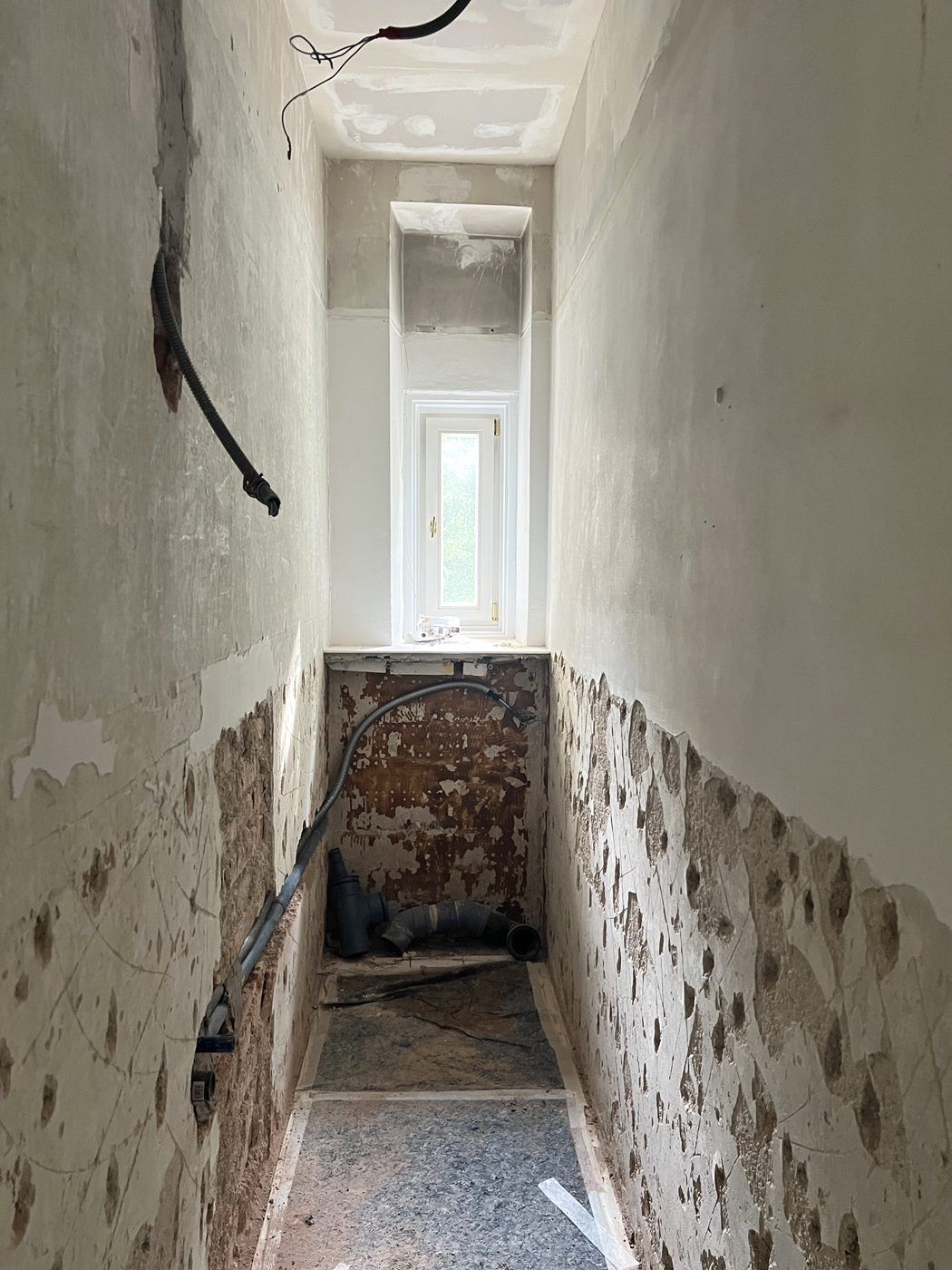 WC-Raum im Rohbau mit Abfluss und Wasserleitung an der Rückwand